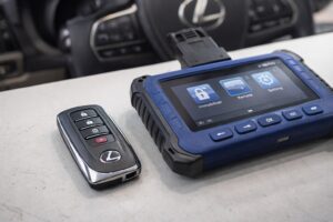 Lexus smart key fob next to a professional key programming tool for OEM vs aftermarket key replacement.